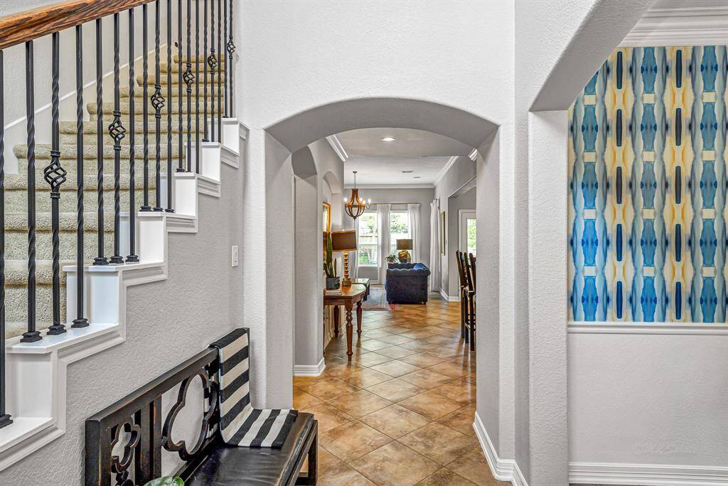 The bright entryway welcomes you with soaring ceilings, gorgeous tile flooring, arched entry and staircase with elegant wrought iron balusters that leads to 4 secondary bedrooms and a game room, ready for family fun.