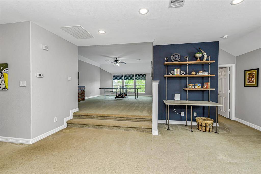 The entryway features soaring ceilings and a view of the dining room and staircase with wrought iron balusters leading to the upstairs game room. Natural light creates a warm, inviting first impression.