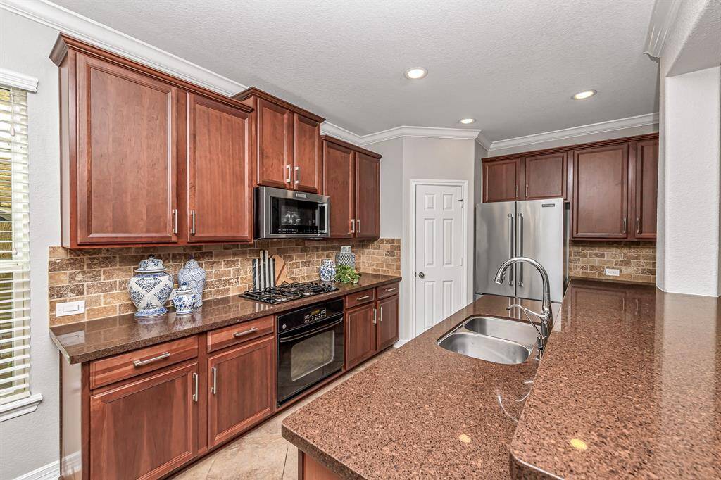 On the back side of the kitchen is a gas cooktop, oven, granite counters, custom brick backsplash and rich colored cabinets.