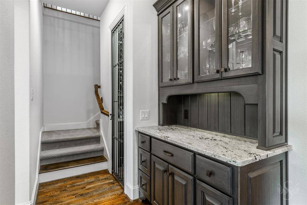 This dry bar is a sleek, stylish space with a polished granite countertop and glass-faced cabinetry, perfect for showcasing glassware. Just beside it, a cozy wine grotto adds a touch of luxury, offering a private spot to store and display your collection.