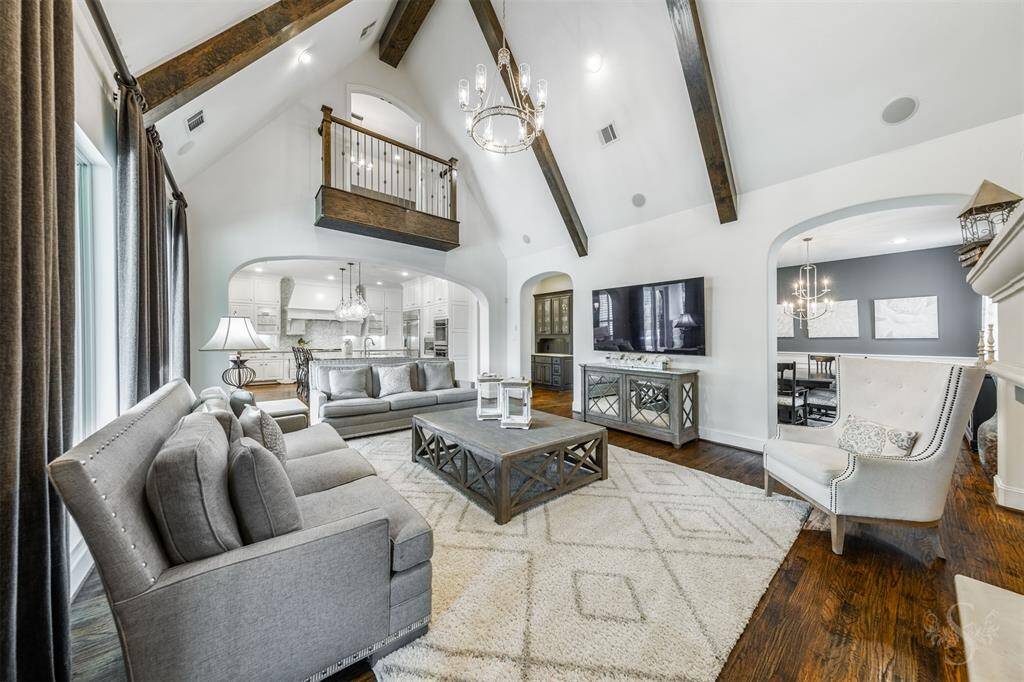 The impressive family room sits beneath a stunning cathedral ceiling with rustic wood beams, creating a warm and inviting atmosphere. An elegant fireplace set against a striking stone display wall serves as the focal point, while large windows flood the room with natural light and offer beautiful views of the outdoor oasis.