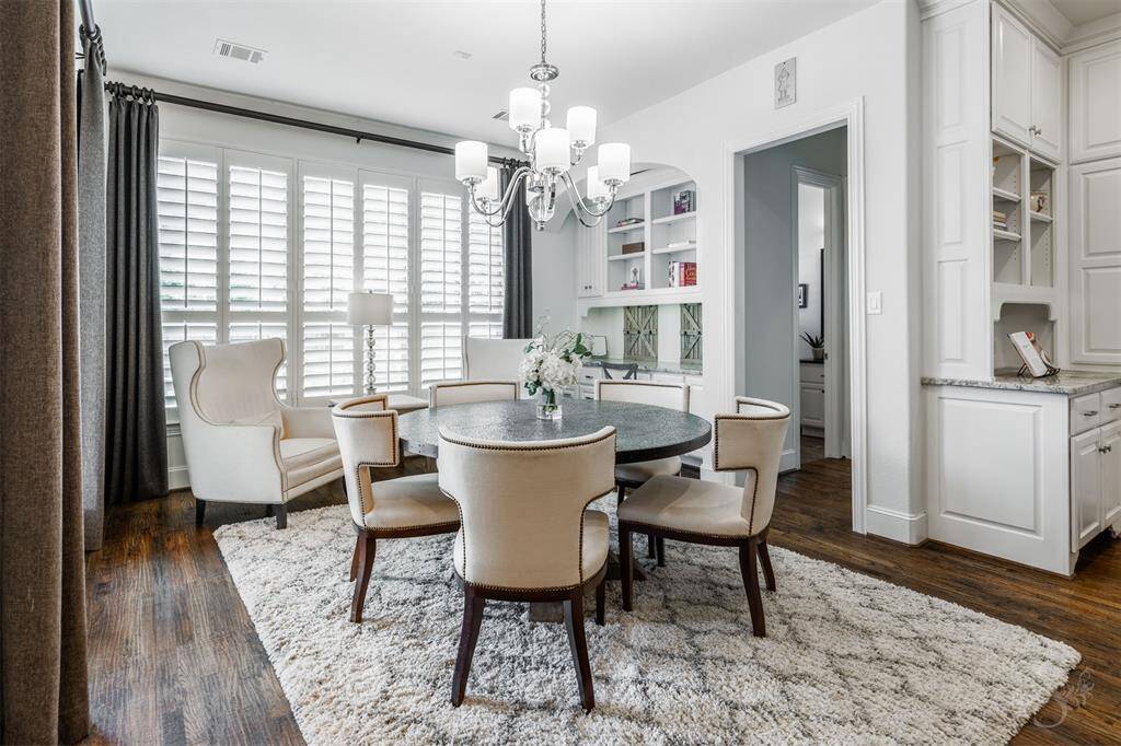 A cozy breakfast room features warm wood flooring and windows with plantation shutters, creating a relaxed and inviting space. It’s the perfect spot for enjoying a morning cup of coffee or a casual meal with natural light pouring in. Note the convenient built-in desk with shelves on the side.