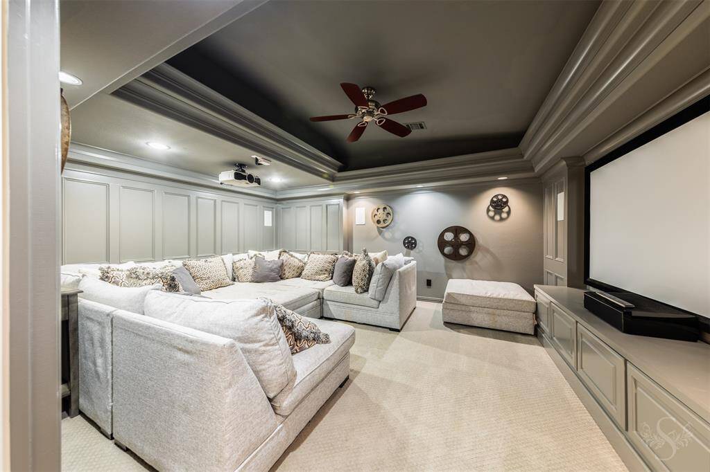 A home media room is designed with custom paint and picture frame wall molding, creating a stylish and inviting space. The impressive tray ceiling with crown molding and built-ins add both elegance and convenience, making it the perfect spot for movie nights and sports games.