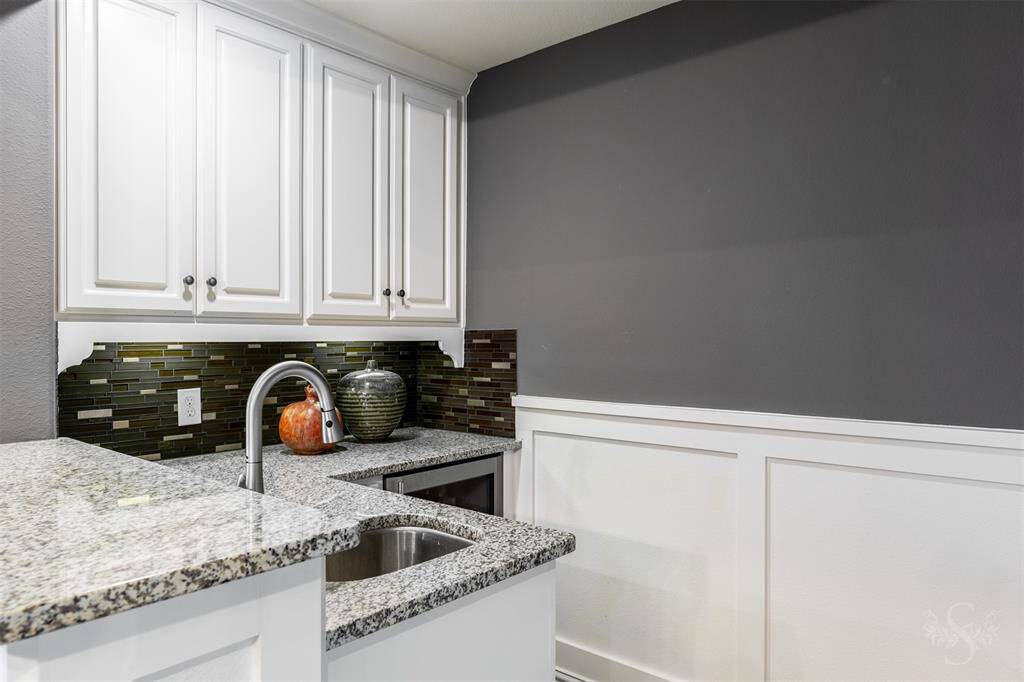 A convenient wet bar, attached to the game room, features a granite countertop and a stylish tile backsplash with some cabinetry for storage making it a great spot for preparing drinks and snacks while enjoying the upstairs entertainment areas.