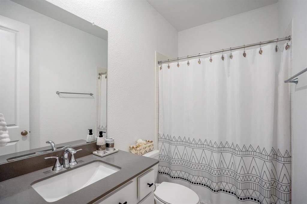 This full bathroom is located just down the private hallway of the first secondary bedroom and is the perfect place for guests to get ready while visiting. It features beautiful quartz countertops, white cabinets, a large mirror, and a spacious combination tub and shower.