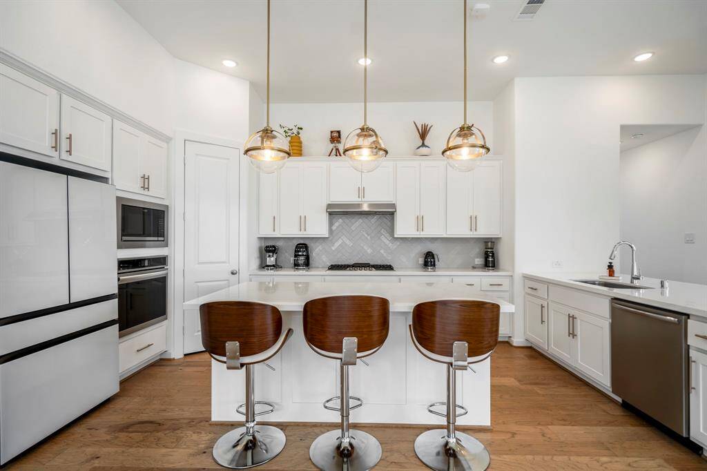 The kitchen boasts a deco wood paneled island with sleek quartz countertops and modern pendant lighting. Upgraded with built-in stainless steel appliances, a 5 burner gas cooktop, and cabinet hardware, this kitchen is ideal for cooking for the whole family or hosting holidays!