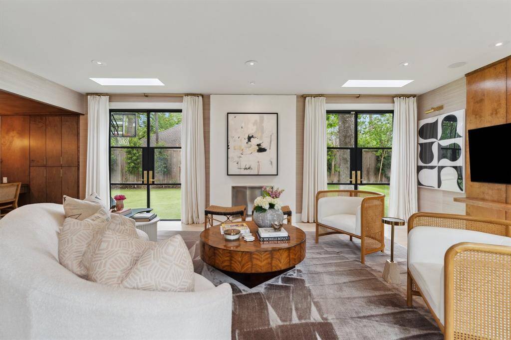 Inviting FAMILY ROOM room with 3 sets of double iron doors opening to the courtyard & expansive side yard. A paneled accent wall frames the TV. The venetian plastered fireplace adds warmth, complemented by recessed lighting and Schumacher grass cloth wallpaper.