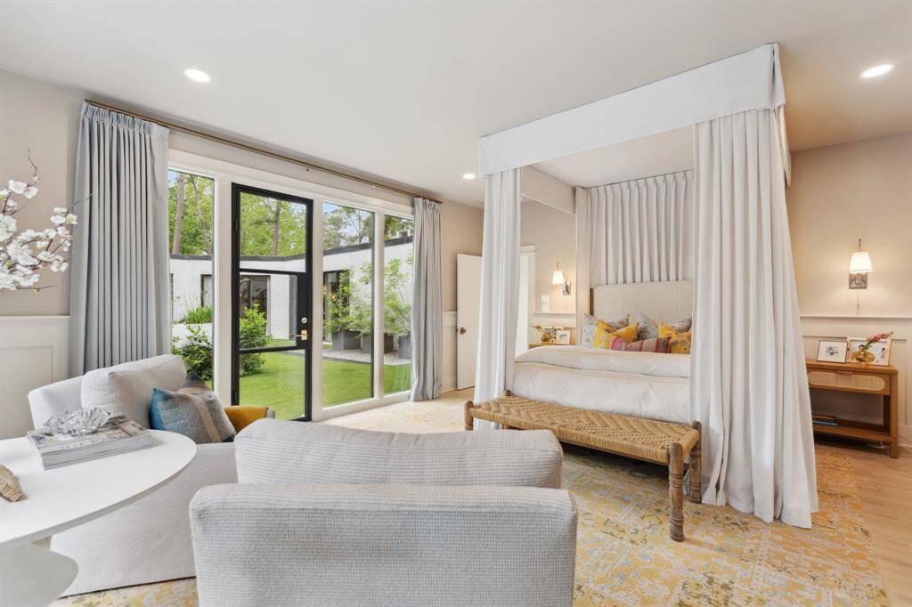This luxurious PRIMARY BEDROOM features oversized windows with custom blackout drapes, a newly added iron door leading outside (April 2025), and elegant wainscotting. Visual Comfort sconces and recessed can lighting provide a warm, inviting atmosphere, while there’s plenty of room for a sitting area.
