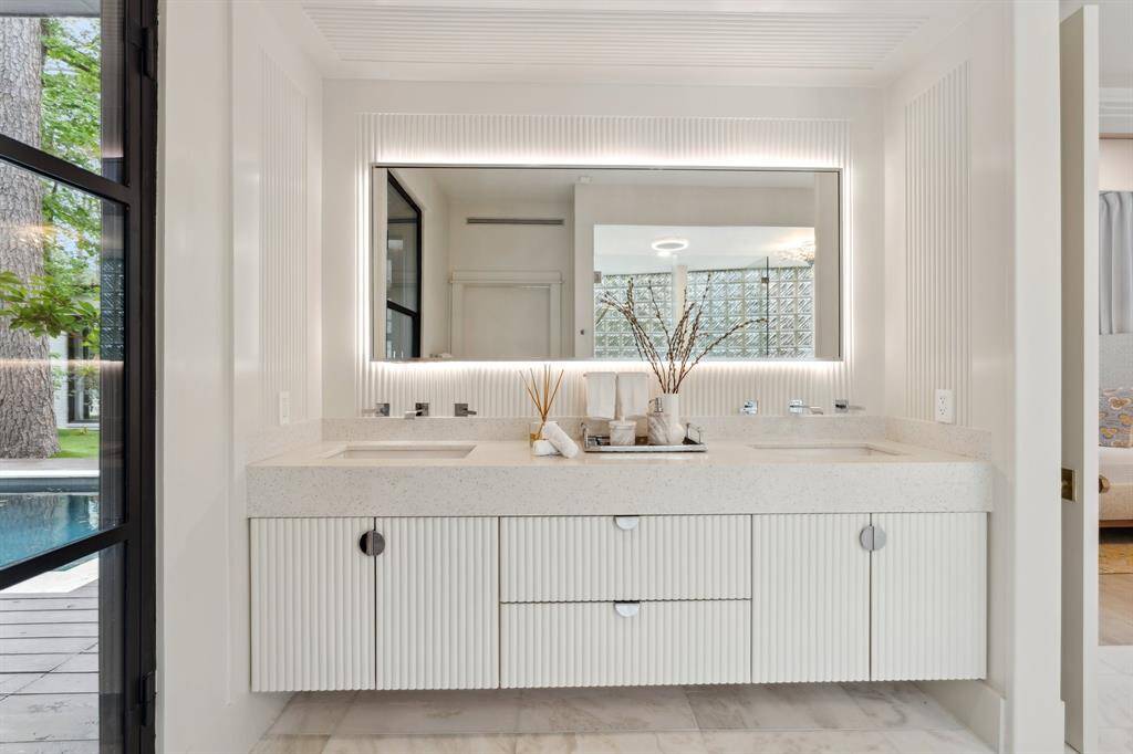 The PRIMARY BATH boasts a floating vanity with dual sinks, a quartz countertop, ample storage, and undermount lighting. A large backlit mirror enhances the space, and another newly added iron door offers easy access to the outdoors (April 2025).