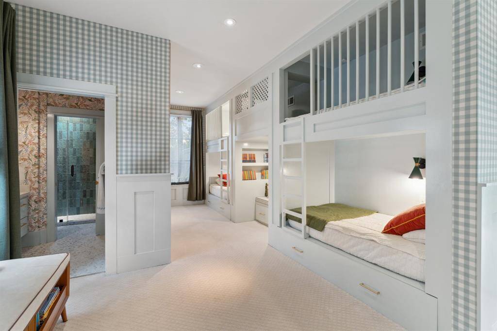 This spacious bunk room sleeps up to six, offering a fun, functional design. The low-profile carpet and lower paneled wall create a cozy atmosphere. Custom-built bunk beds feature a reading nook below and a hidden play area above, with sconces and outlets on each twin bunk. Two pull-out trundles provide extra space for the ultimate slumber party. Recessed lighting, steel windows, and sheer pull-down drapes with black-out curtains add to the room's charm.