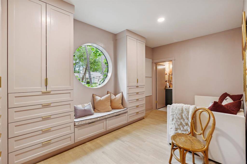 This versatile space can serve as a study, flex room, playroom, or guest bedroom #4. A large circular window offers glimpses of ivy creeping through, framing serene views of the wooded front yard. A custom bench seat with a cushion beneath and built-in cabinetry with brass hardware and slow-close drawers provide ample storage while adding charm to the room.