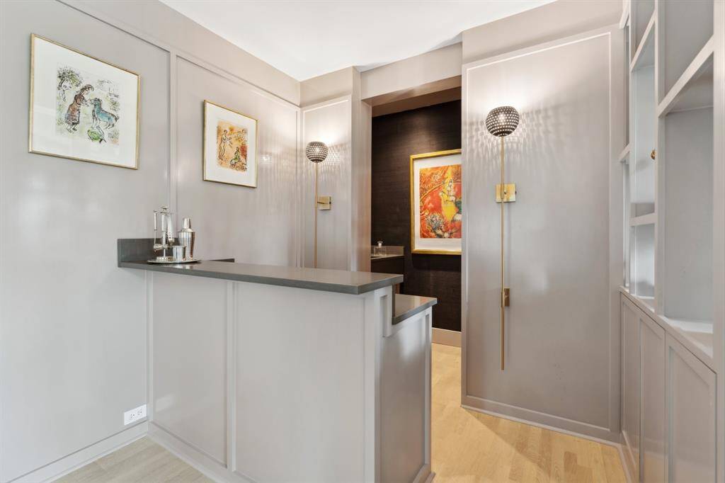 The entertainer’s bar features an open serving area and a sleek back bar, complete with a large stainless-steel wine fridge. A built-in vanity with a sink adds convenience, while Schumacher wallpaper lining the back wall enhances the space with a refined touch. Perfect for hosting, this bar seamlessly blends into the home’s elegant design.