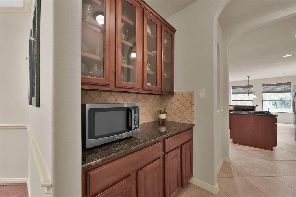 A Butler's Pantry connect the Kitchen to the Dining Room and has glass-front upper cabinets to display pretty dishes and additional lower cabinets for extra storage with a granite countertop. The seller is including the microwave with the sale. An art niche is located to the left in between the arches. To the right you will find the Laundry Room and the Primary Bedroom at the end of a private hallway.