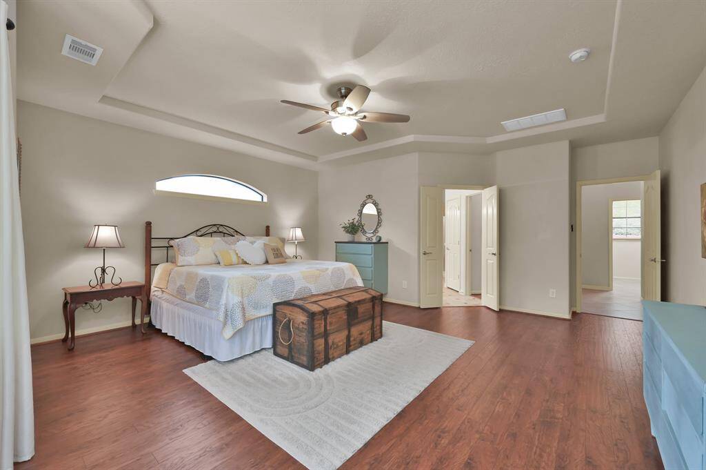 The spacious Primary Bedroom is secluded and private off a hallway from the Kitchen. It has a tray ceiling, crown molding, wood laminate floors installed in 2023 and a ceiling fan to keep cool. The arched window over the bed adds architectural detail.