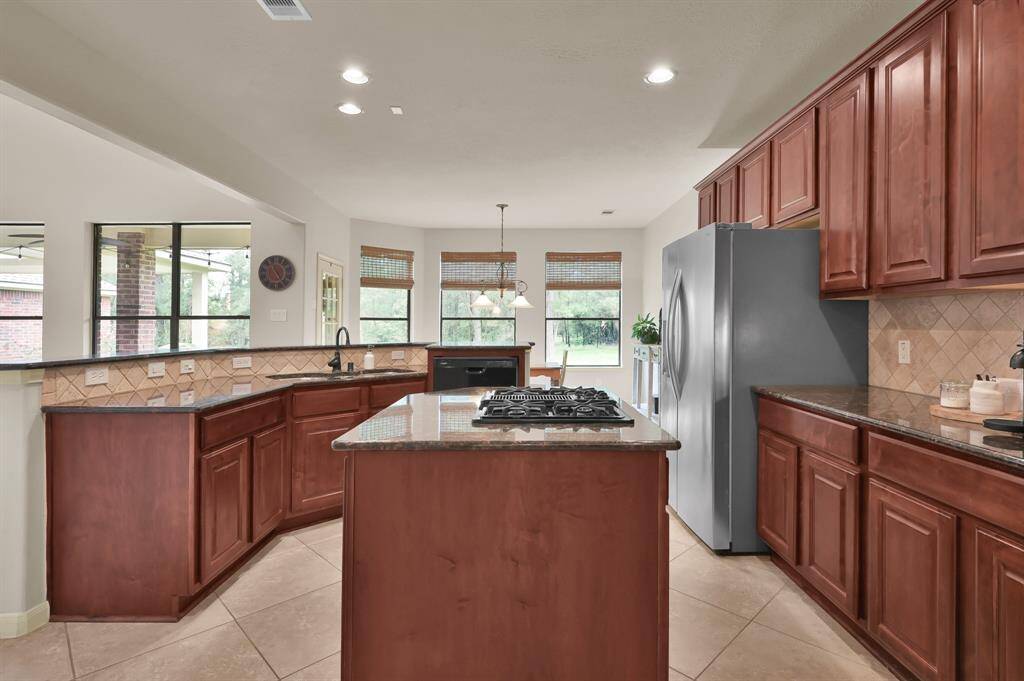 A gas stove built-in to the island makes a chef happy and cleanup is easy in the triple-basin stainless steel sink with oil rubbed bronze faucet and recently replaced Whirlpool dishwasher (2024). Beyond the Kitchen is the Informal Dining Area with Rattan Roman shades on three windows and a door to the back covered patio.