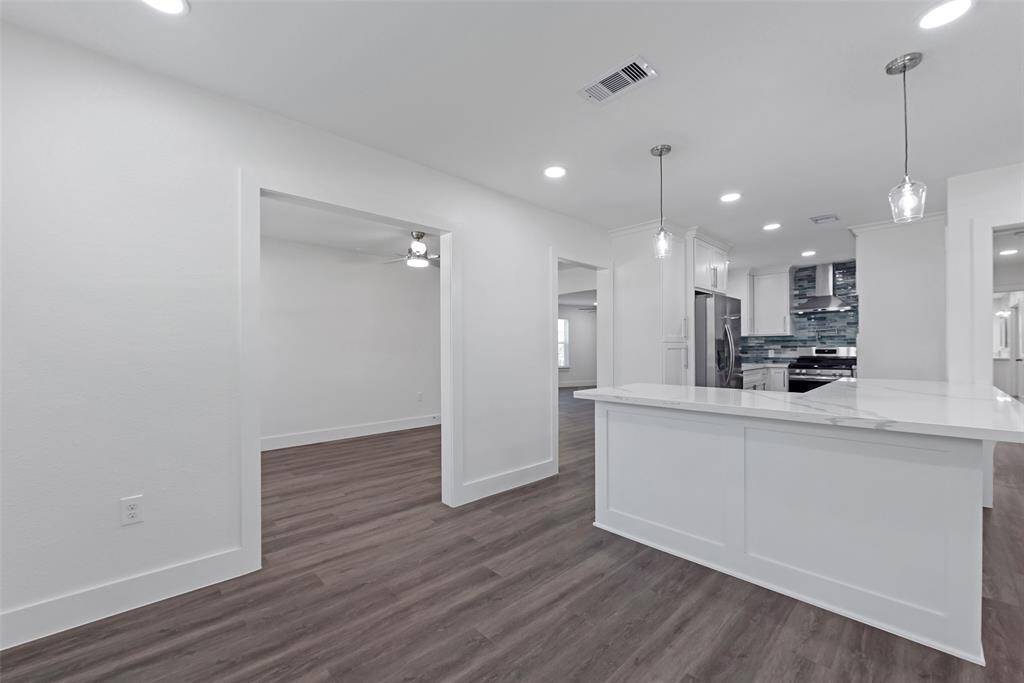 This photo showcases a modern, open-concept kitchen with sleek white cabinetry, a large island, and stainless steel appliances. The space features recessed lighting, pendant lights, and dark wood-style flooring, creating a bright and contemporary atmosphere.