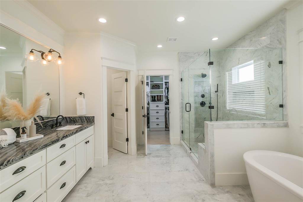 This bathroom features a modern design with a spacious glass-enclosed shower, a freestanding bathtub, and a double vanity with elegant countertops.  A walk-in closet is accessible through a doorway.