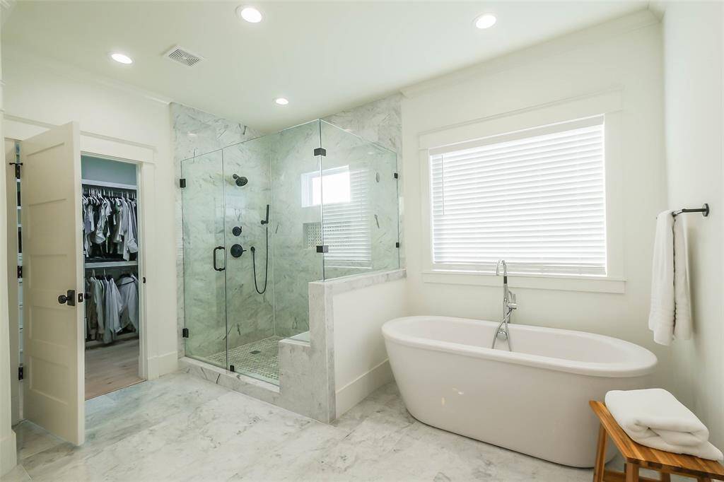 Wonderful frameless glass step-in shower, a sleek freestanding bathtub, and elegant flooring. Note the spacious walk-in closet, offering convenience and luxury.