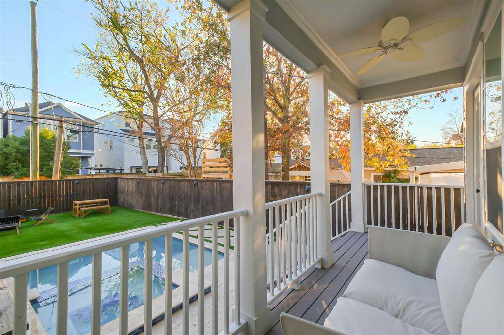 This photo showcases a cozy porch with white railings and a ceiling fan, overlooking a fenced backyard with a pool and artificial turf creating the perfect outdoor space.