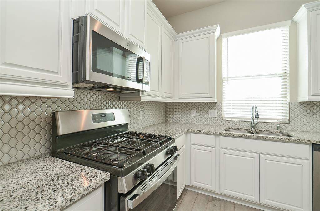 Kitchen features granite countertop with complementing backsplash.  Stainless steel gas range, microwave and dishwasher