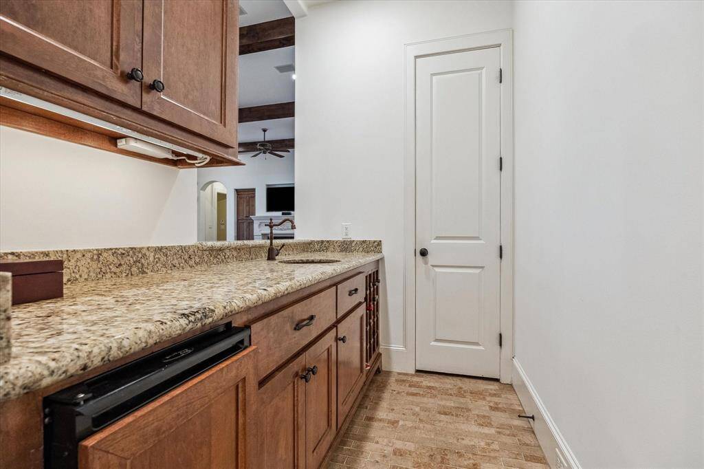 This well-appointed bar area features granite countertops, custom cabinetry for ample storage, and a built-in under-counter refrigerator for convenient beverage access. A small prep sink and dedicated wine storage add functionality, while the space connects easily to the adjacent living area, making it ideal for entertaining.