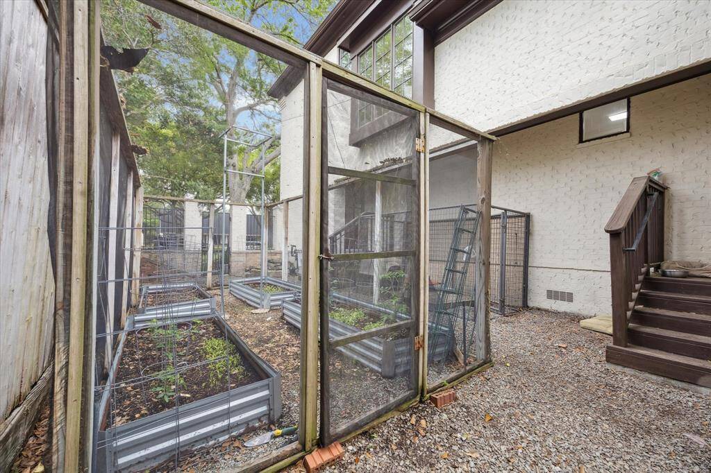 This herb garden is enclosed with a screened structure for protection and features several raised beds filled with soil. It includes support structures for vertical growth and is situated on a gravel surface beside the house.