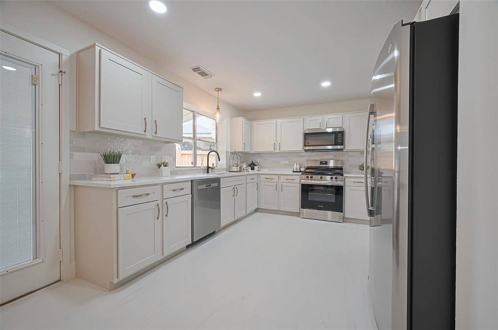 Remodeled kitchen features new cabinetry painted in Natural Cream by BM, Calacatta gold quartz counters, upgraded tile, designer backsplash, new appliances, new farmhouse sink & fixture, designer hardware & chic lighting!