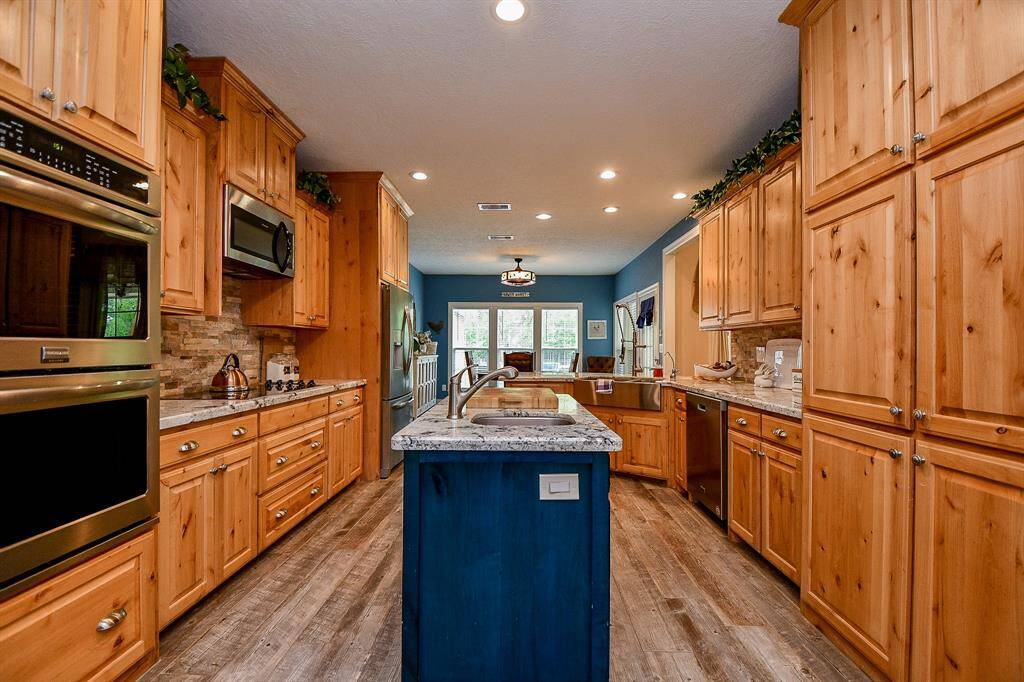This spacious kitchen features rustic wooden cabinetry, stainless steel appliances, and a central island with a granite countertop. The open layout flows into a well-lit dining area, creating a warm and inviting atmosphere.