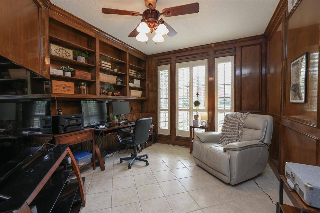 The home office has beautiful wood paneled walls and tile flooring.  Built in desk & shelving, ceiling fan, plantation shutters and tile flooring.