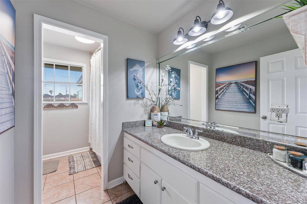 This bathroom offers a spacious granite-top vanity, stylish fixtures, and natural light for a fresh and airy feel.