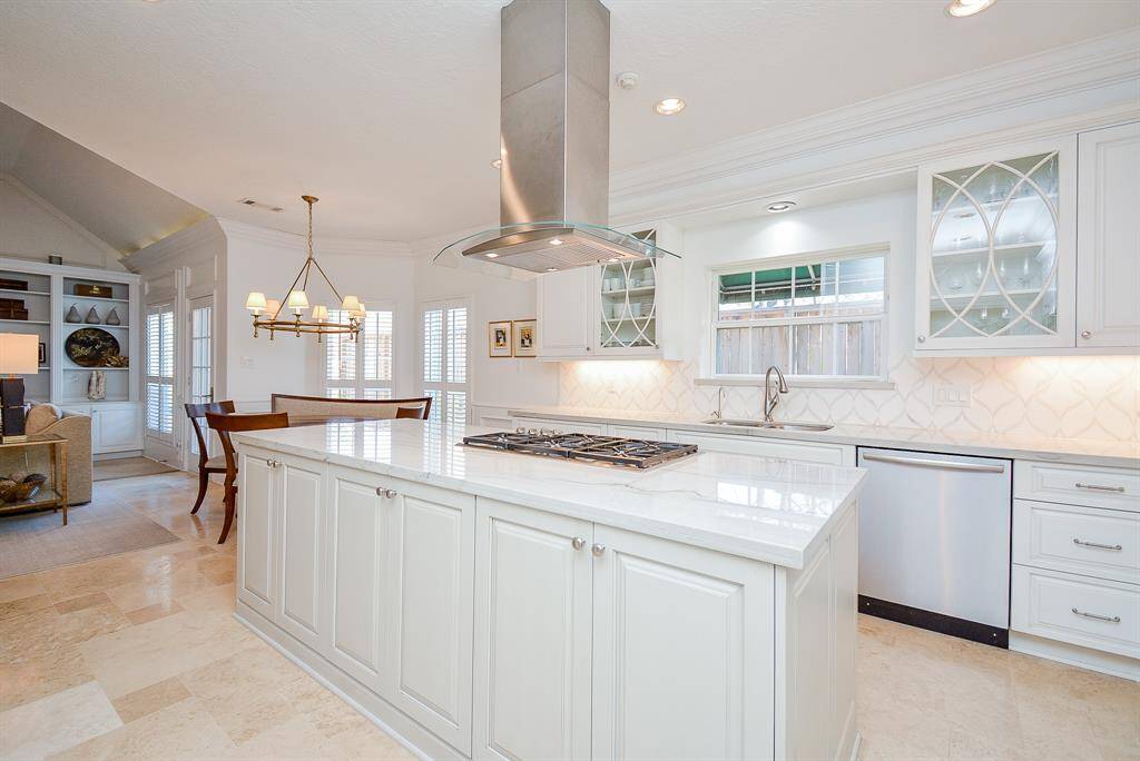 This photo showcases a bright, Open-Concept Kitchen and Casual Dining area with a Large Central Island, Gas Cooktop, Modern Stainless Steel Range Vent, Elegant Cabinetry with Undermounted Lighting and Quartzite Coubtertops.