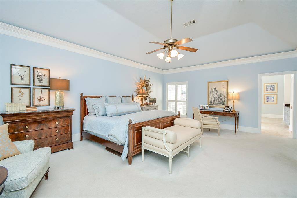 The Spacious Primary Bedroom with plenty of room for a desk and a seating area features a High Ceiling, Ceiling Fan and Crown Molding Creating a serene atmosphere.