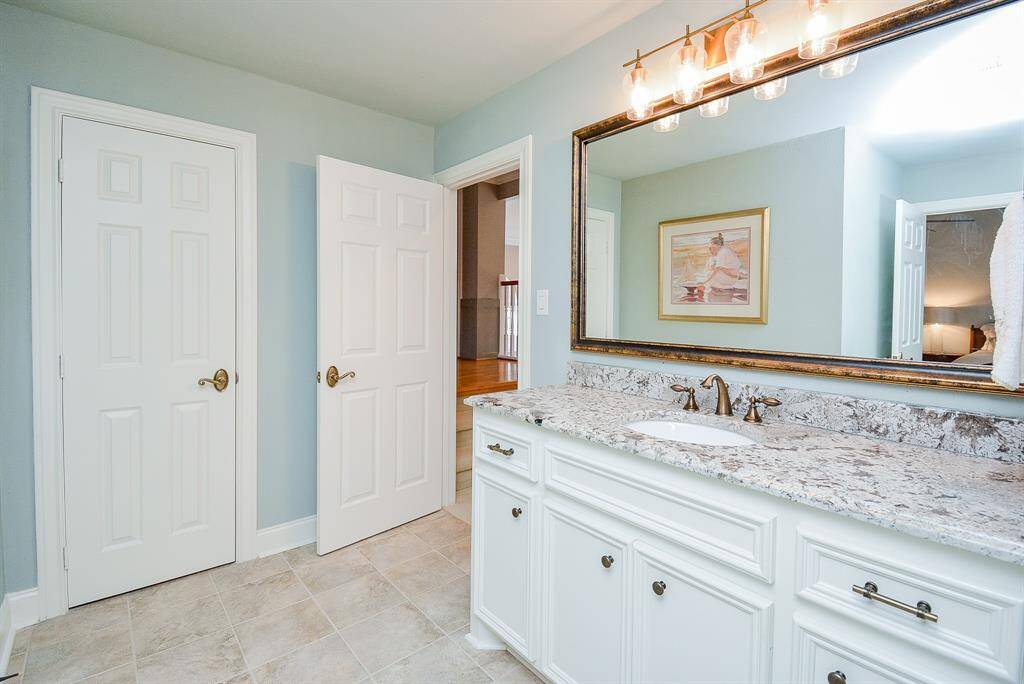 Here is another bathroom that also features a spacious vanity with a large mirror and elegant lighting. The granite countertop adds a touch of luxury, complemented by white cabinetry.