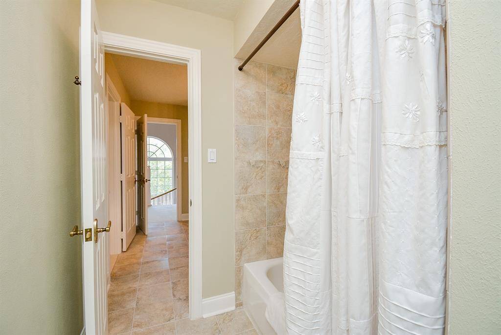 This photo shows a bright bathroom with a modern tiled shower and bathtub and another door that opens to the hallway.