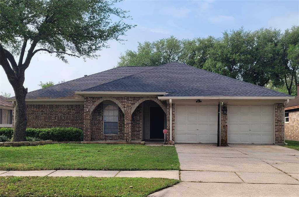 Charming single-story brick home with a dark shingled roof and a two-car garage. The front features arched windows and a well-maintained lawn with mature trees, creating a welcoming atmosphere.
