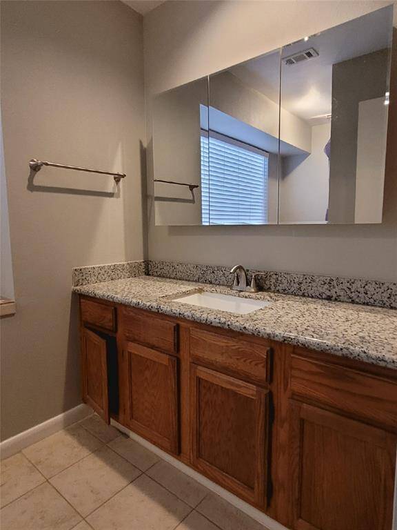 This bathroom features a granite countertop with a single sink, wooden cabinetry, and a large mirror. It has a neutral color scheme with tile flooring and a window for natural light.