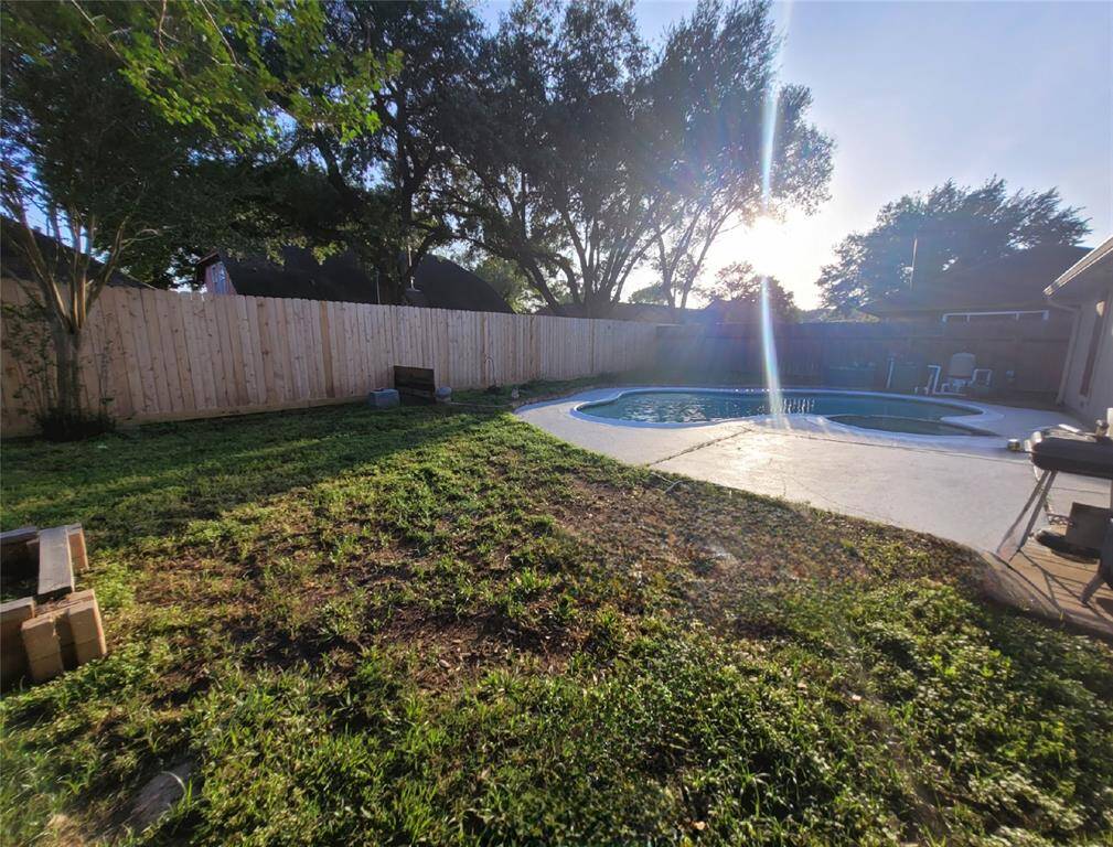 This backyard features a spacious area with a swimming pool, surrounded by a wooden fence for privacy. There is ample lawn space for activities, and mature trees provide shade. Ideal for outdoor entertainment and relaxation.