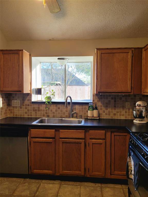 This kitchen features warm wooden cabinets, a modern tile backsplash, and a spacious window above the sink for natural light. The dark countertops offer a sleek look, complemented by sleek appliances.