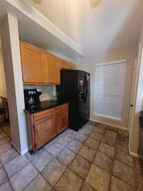 The photo shows a cozy kitchen corner with tiled flooring, featuring wooden cabinets. A large window with blinds allows natural light in.