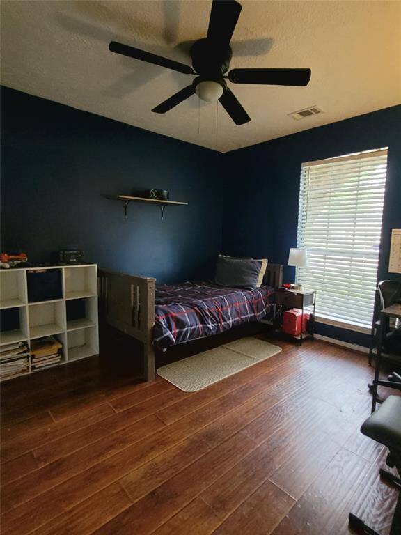 Cozy bedroom with dark blue walls and wooden flooring. Ceiling fan for comfort and natural light brightens the space.