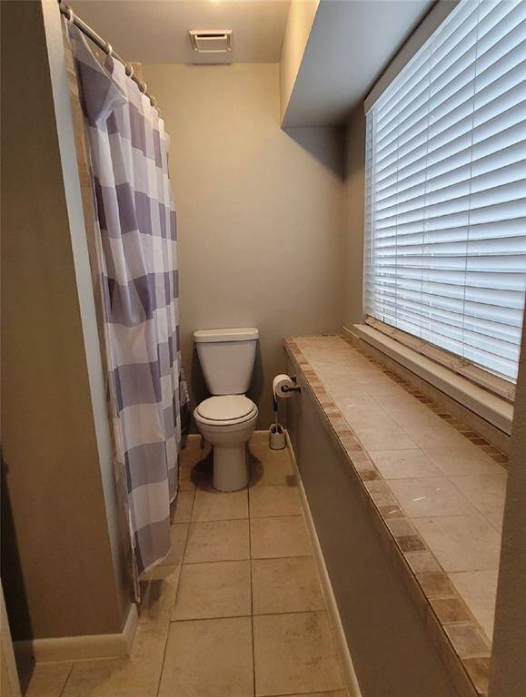 This bathroom features a large window with blinds and a tiled ledge, providing natural light and additional space. The neutral tones create a clean and simple atmosphere.
