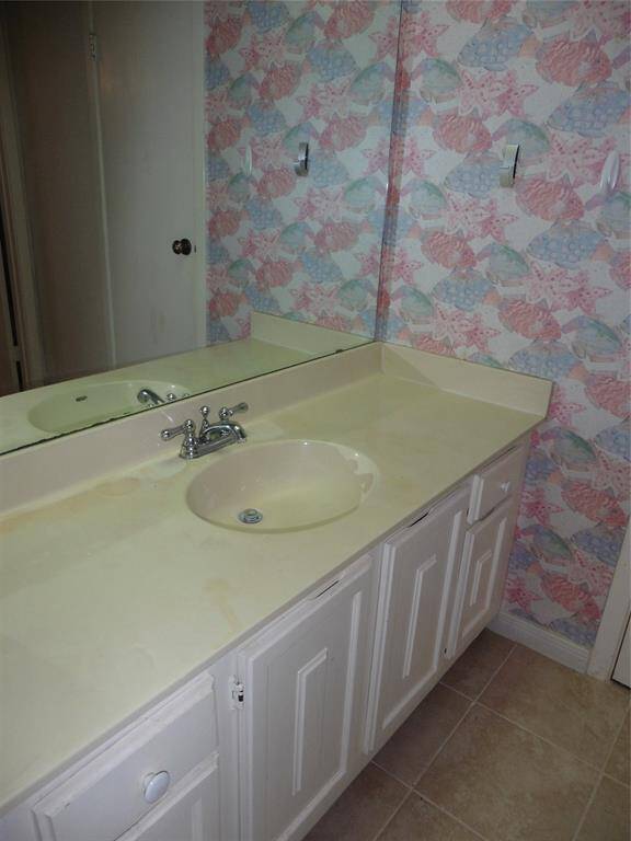The guest bathroom features a single sink vanity with a vintage-style faucet, white countertop, and floral wallpaper. The room includes a large mirror and tiled flooring, providing a classic look.