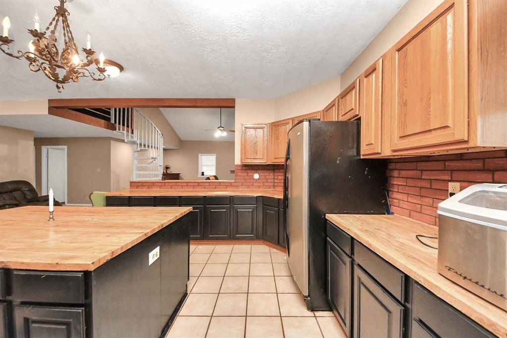 This photo showcases a spacious kitchen with wooden cabinetry and black accents, featuring a central island and stainless steel appliances. The space includes a spiral staircase and a decorative chandelier, enhancing its charm.