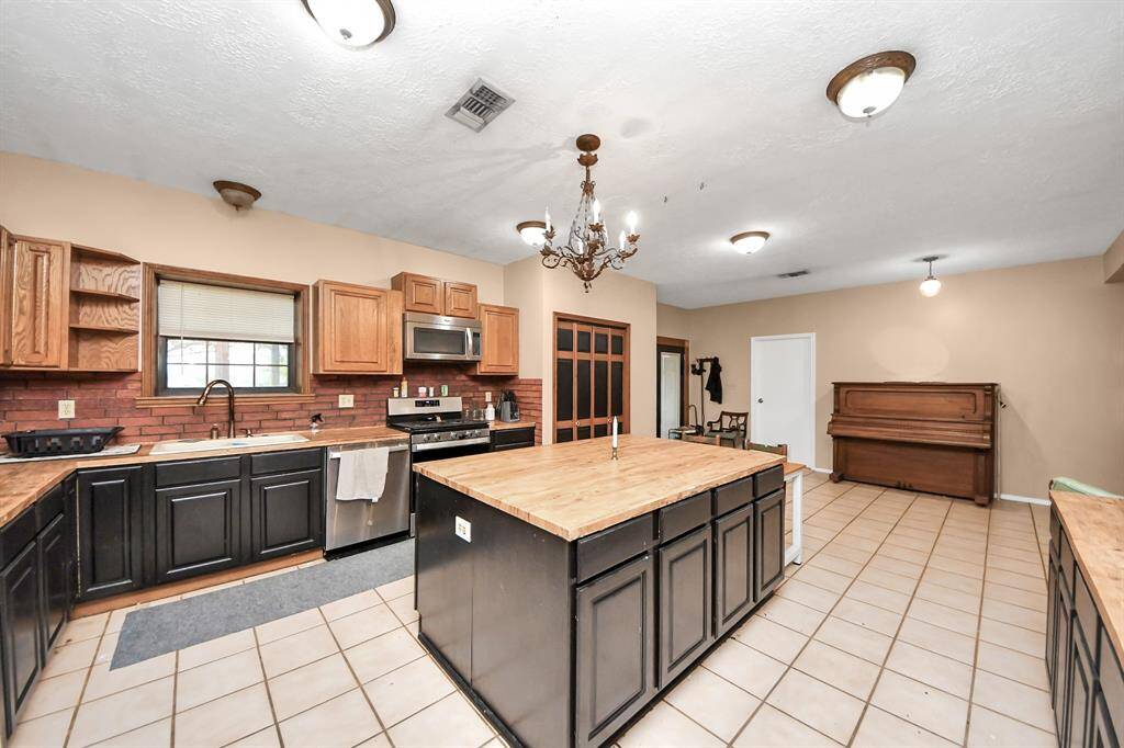 Spacious kitchen with a central island and ample counter space, featuring a blend of wood and dark cabinetry. It includes stainless steel appliances, a chandelier, and a cozy dining area. Perfect for entertaining and family gatherings.