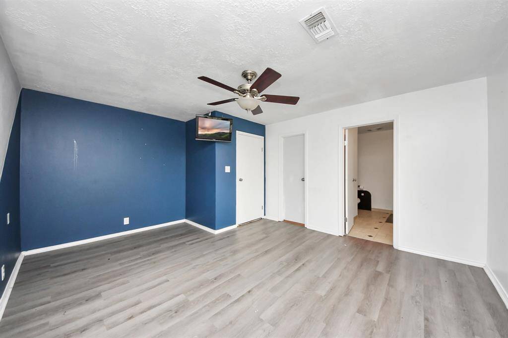 This room features a modern look with sleek gray flooring and a bold blue accent wall. It includes a ceiling, with two doors leading to a bathroom and another room, offering functionality and style.