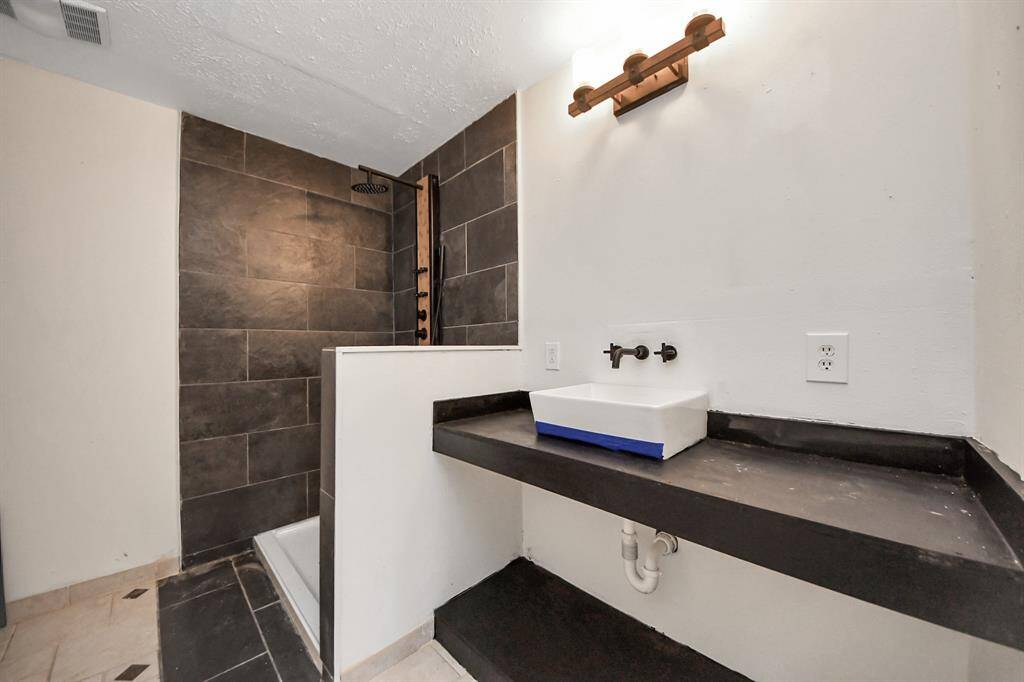 Modern bathroom with a sleek design featuring a walk-in shower with dark tiles, a minimalist rectangular sink, and dark countertop. Bright lighting adds a clean and contemporary feel.