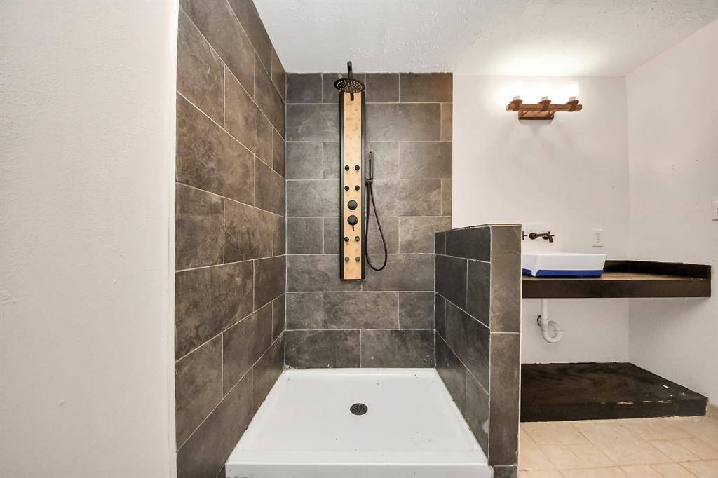 This bathroom features a modern walk-in shower with sleek dark tiles and a stylish wooden shower panel. The space includes a contemporary floating sink with a minimalist design and warm lighting, creating a cozy and functional atmosphere.