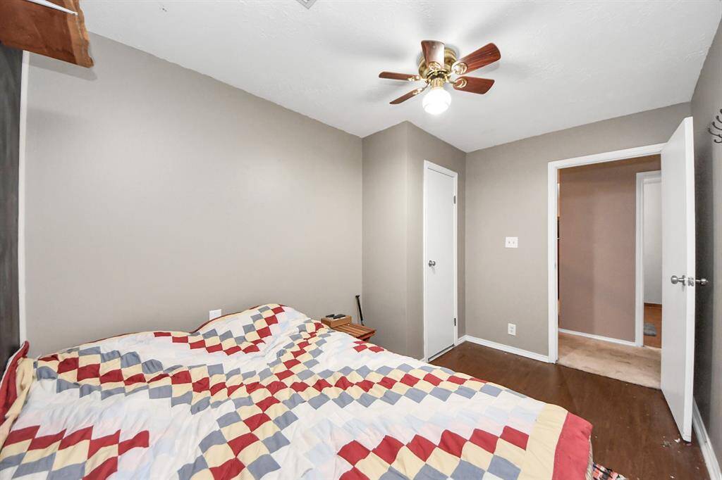 Cozy bedroom with neutral walls and wood flooring, featuring a ceiling fan and access to an adjacent room. Perfect for creating a comfortable personal space.