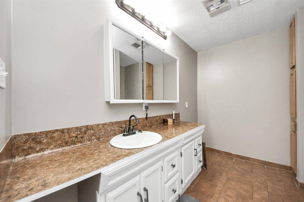 This bathroom features a spacious vanity with a marble countertop, a large mirror, and ample under-sink storage. The neutral tones and tiled flooring create a clean and inviting atmosphere.