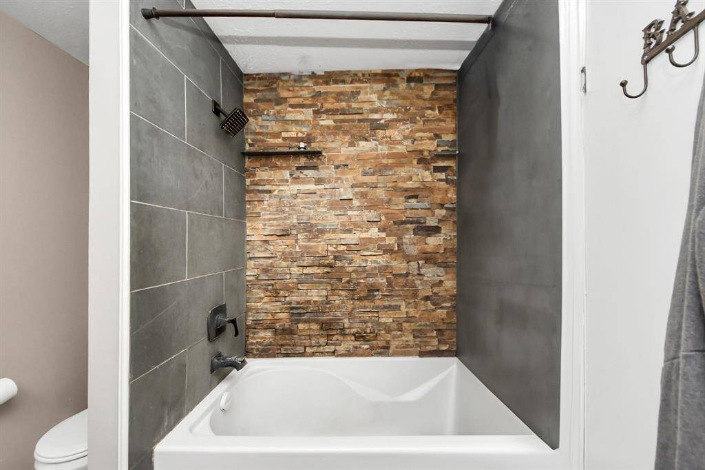 Modern bathroom featuring a bathtub with a sleek gray tile and stone accent wall, offering a stylish and rustic look.
